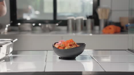 agregando rábano en escabeche al tazón de salmón y atún en el mostrador de la cocina