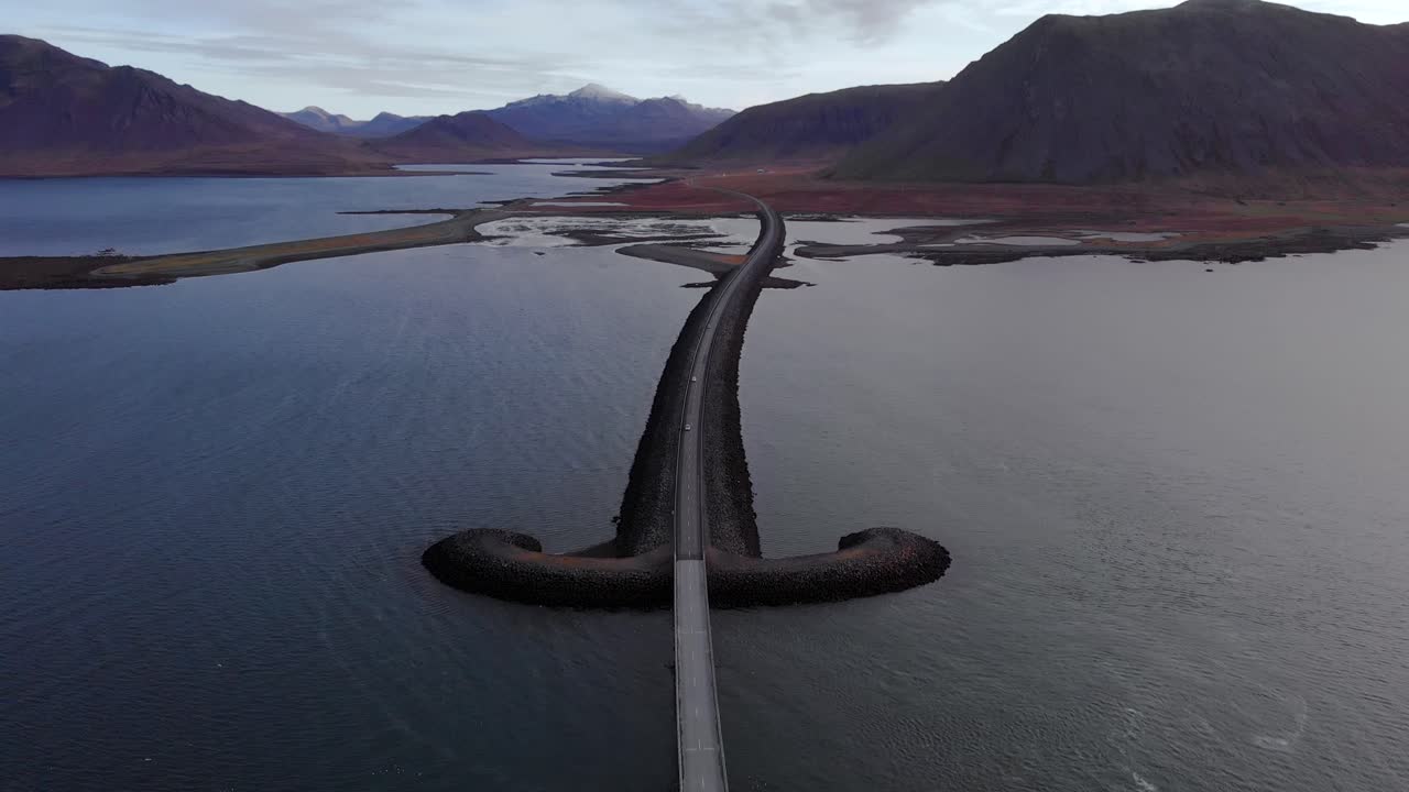 vista aérea en 4k sobre una carretera islandesa con forma de espada sobre el océano, rodeada de paisajes montañosos, islandia, europa, inclinación hacia arriba para establecer la toma