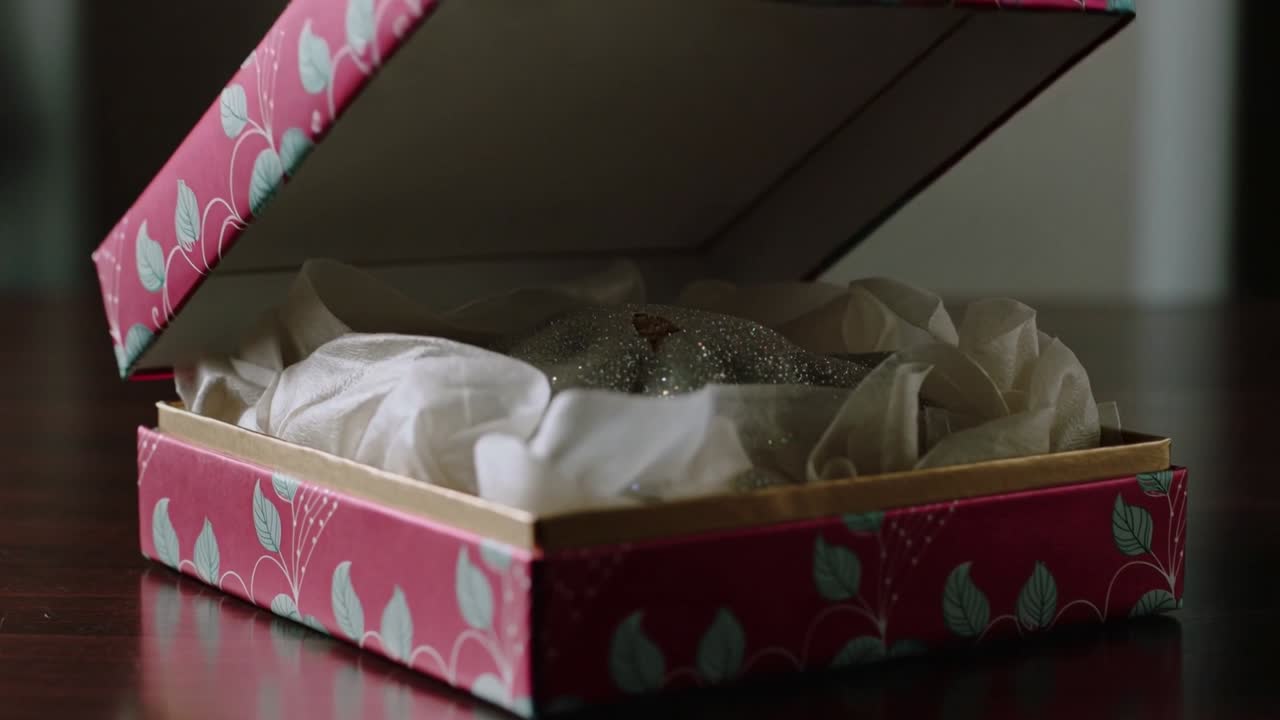 Lid lifting from pink gift box revealing silver glittered pumpkin on wooden table, showcasing decor