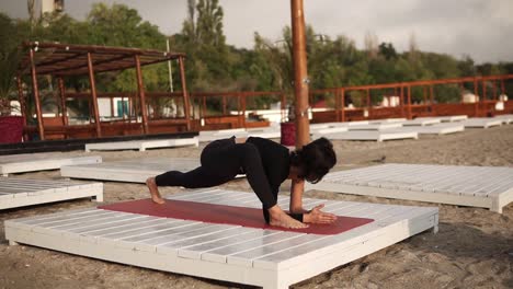 Woman-Practicing-Yoga-On-Mat-On-The-Beach-Performing-Yoga-Or-Stretching-Legs,-Performing-Extended-Side-Angle-Pose