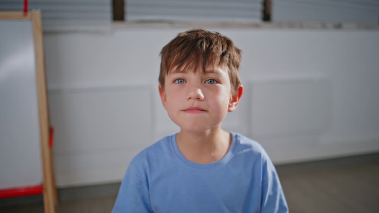 Small boy raising hand at lesson closeup. Smiling pupil learning at school room