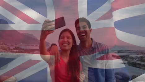 animación de la bandera del reino unido sobre una pareja feliz y diversa tomando selfies en el mar