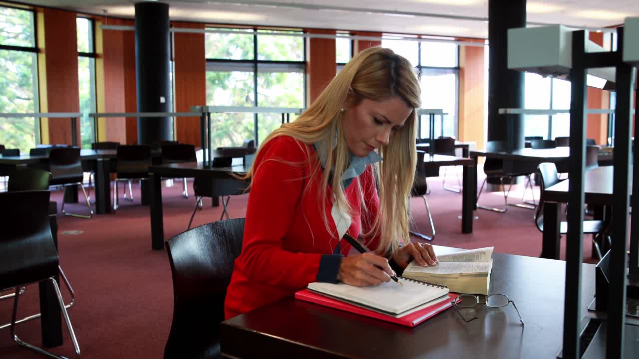 Voksen student med lesebriller som studerer ved et bibliotekbord