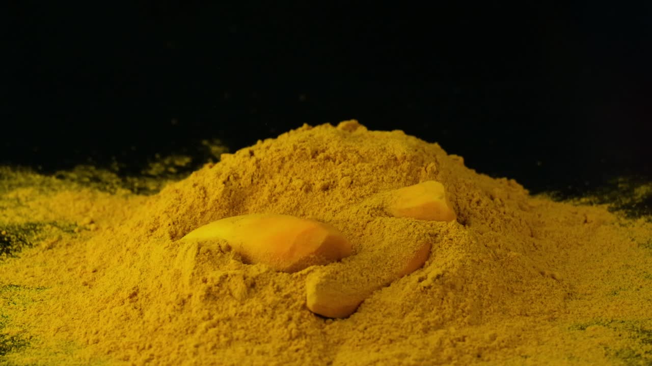 Stücke geschälter Kurkuma-Rhizome fallen auf einen Haufen Kurkumapulver.