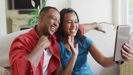 happy biracial couple sitting on sofa, and having video call on smartphone
