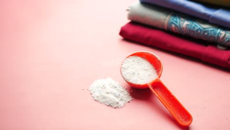 detergente para la ropa en cucharada naranja sobre fondo rosado