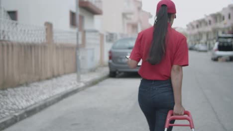 Female-delivery-worker-wheeling-cart-with-parcels