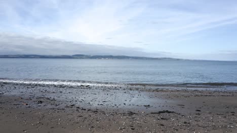 calm waves on a beach looking across the water to an island | edinburgh, scotland | 4k at 30 fps