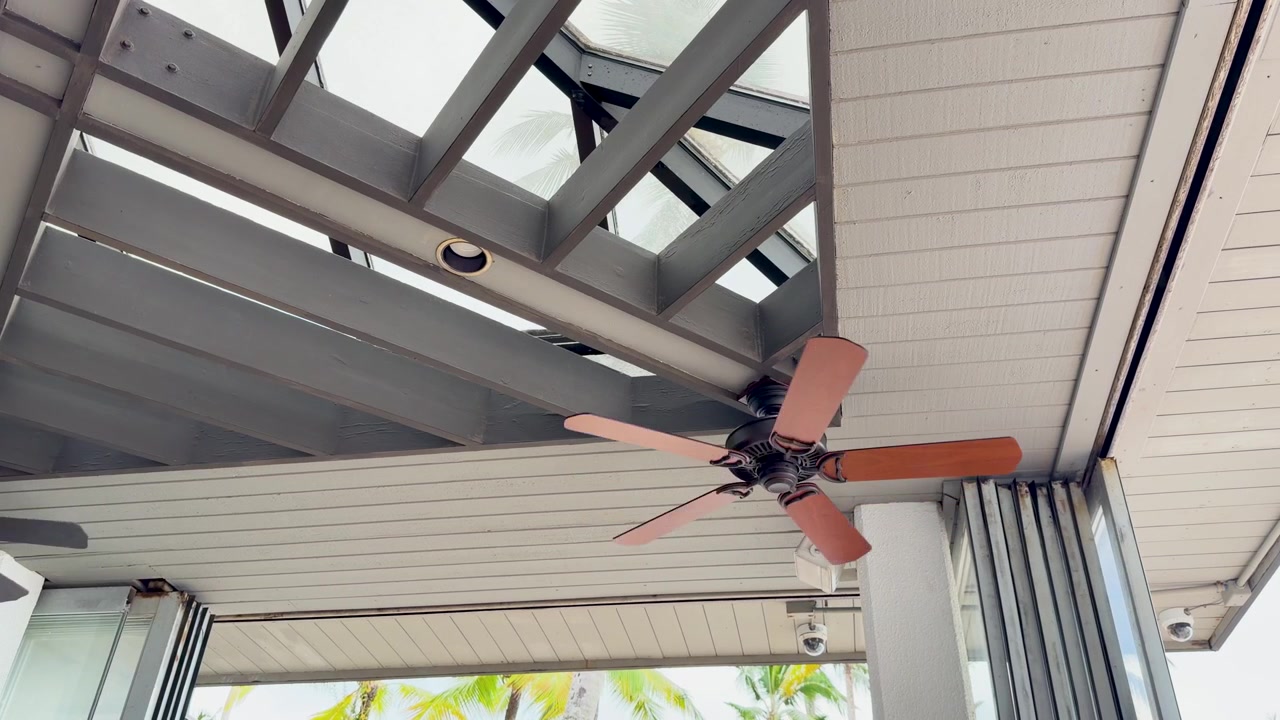 A low angle shot of a wooden ceiling fan rotating under a modern pergola roof