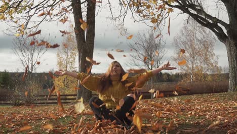 adult girl is throwing leaves sitting under the trees with autumn colours