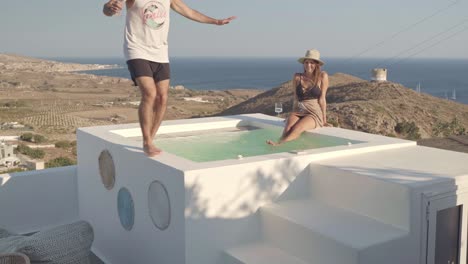 young-couple-enjoy-wine-at-rooftop-spa-while-man-balances-on-the-edge-of-the-hot-tub-retrieving-more-drinks