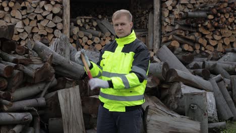 lumberjack in reflective jacket. man woodcutter with small axe. sawn logs, firewood background