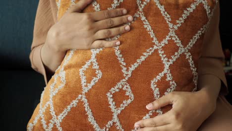 close-up of a woman's hands holding a decorative pillow on a couch