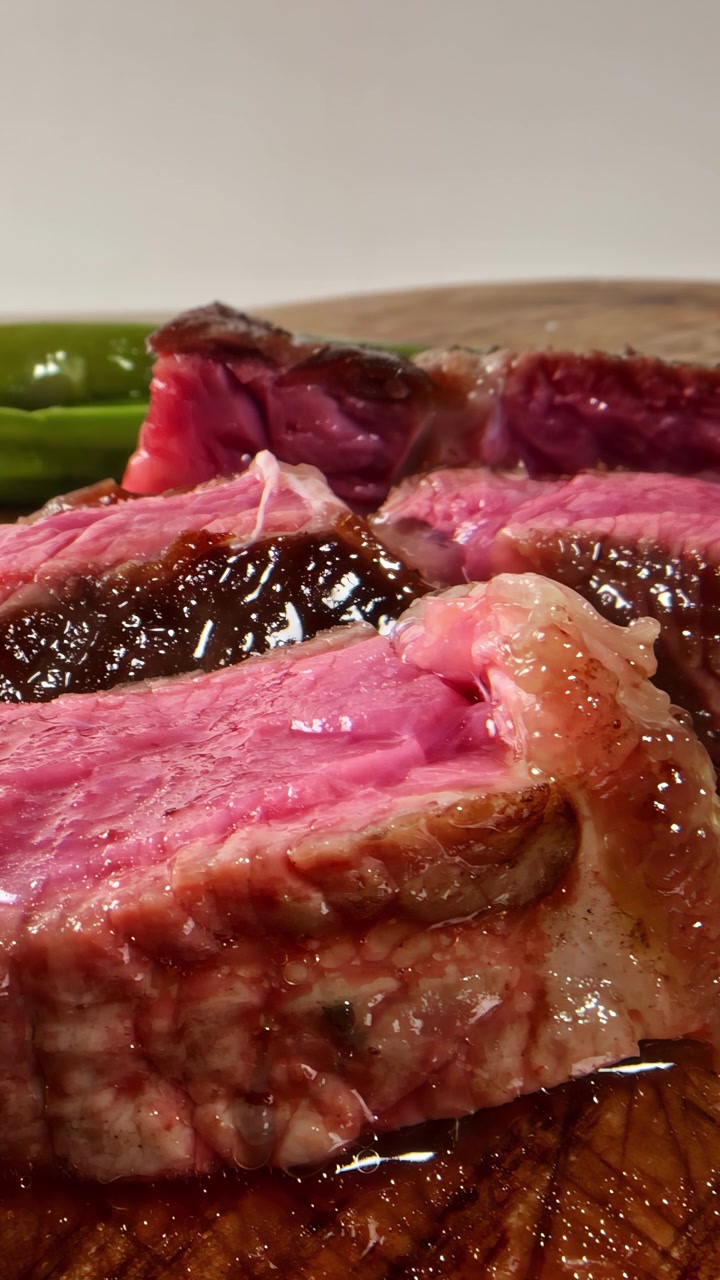 Primo piano di succulente fette di bistecca al sangue su un tagliere di legno, che mostrano una ricca marezzatura e i succhi. Ideale per blog culinari e tutorial di cucina