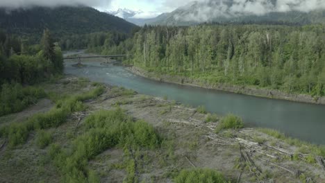 Drohnenaufnahmen-Des-Wunderschönen-Pazifischen-Nordwestflusses,-Des-Nebligen-Waldes-Mit-Brücke-Und-Bergen-Im-Hintergrund