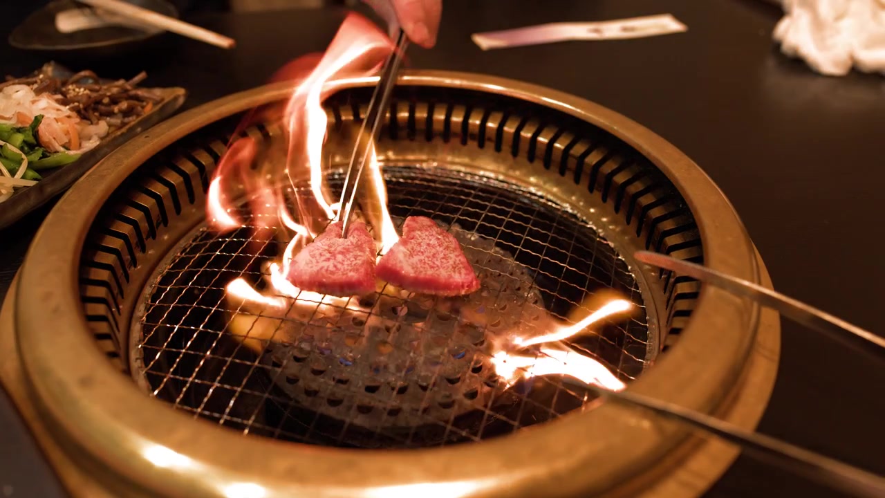 Fette di manzo pregiato cuociono su una griglia a carbone con fiamme che si alzano in un ristorante