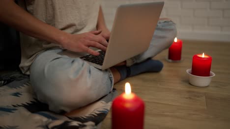 cropped footage of a woman working on modern laptop while sitting in a cozy room around candles