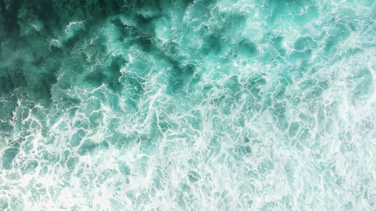Drone quick ascend top down from waves breaking on shallow fringing reef in ocean water
