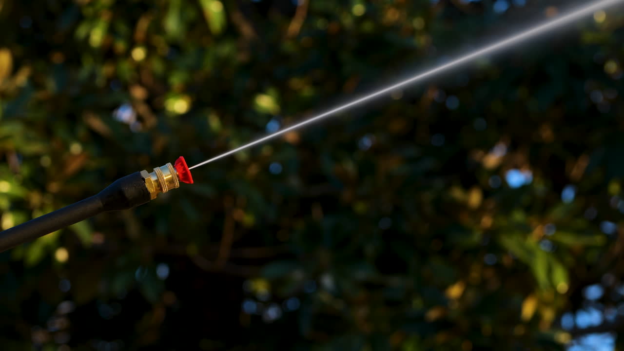 Power washer with red tip sprays high powered water jet with trees in background
