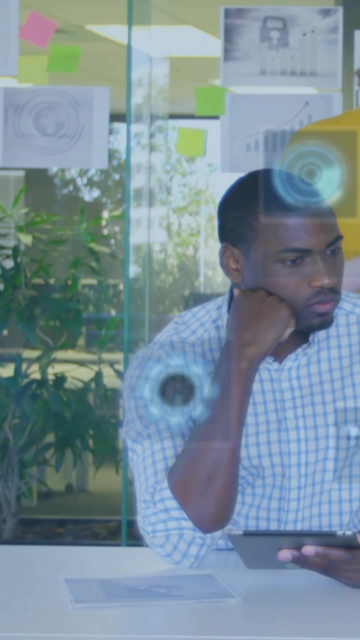 Vertical video: Seated man with tablet, glancing right then back, growing HUD on glass for tech