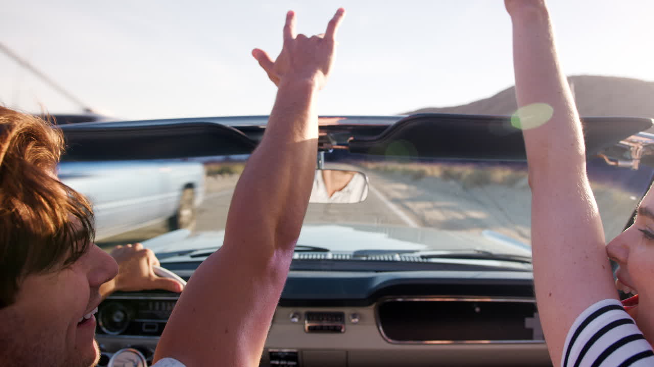행복 한 커플 이 손 을 높이 들고 열린 차 를 운전 하고 있다