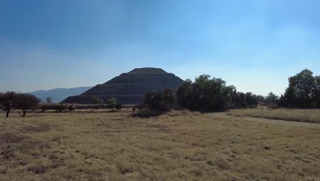 Stunning-view-of-one-of-the-iconic-pyramids-in-Teotihuacan,-Mexico-surrounded-in-nature-and-set-against-a-breathtaking-vibrant-blue-sky