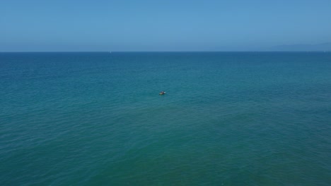 Flying-above-a-vacation-kayak-canoe-boat-in-blue-clear-water-seaside-bay-in-the-idyllic-mediterranean-sea-ocean-by-the-Tuscany-coast-with-blue-sky