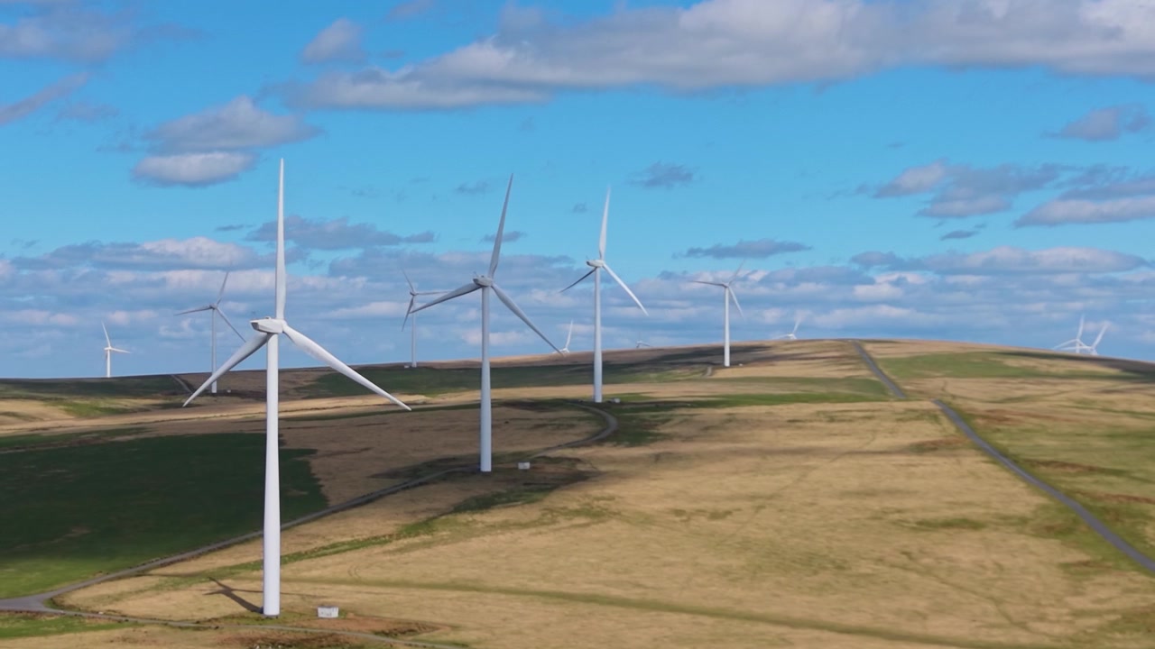 Slow Sideways Aerial of Wind Turbines Spinning and Facing in Same Direction. Drone Clip of Renewable Energy Generation Infrastructure in UK. 4K.