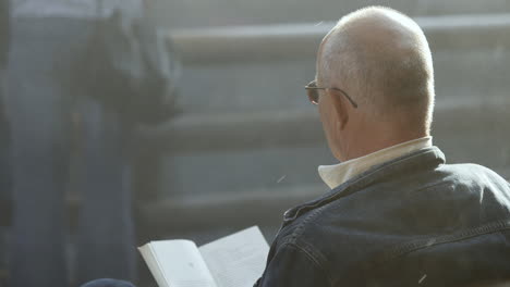 close up shot of an elderly gentlemen relaxing reading a book at a landmark graduation tower in poland with salt water mist passing by