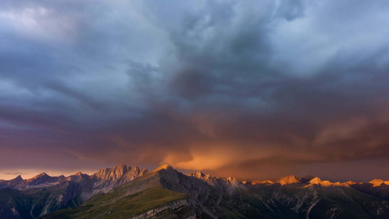 Dramatic Mountain Ridge At Sunset, Stormy Sky Rolling Above Sunlit Alpine Peaks, Warm Golden Light Kissing