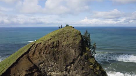 Turistas-Haciendo-Caminatas-Subiendo-Una-Colina-Costera-Hacia-La-Cumbre-Con-Vista-Al-Océano-Turquesa,-El-Pulgar-De-Dios,-Costa-De-Oregon,-Vista-Aérea-Estática