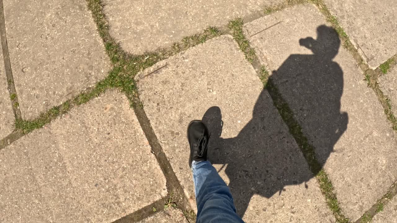 Young man walking on old concrete pathway with shadow on ground, POV