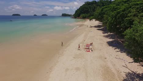 tropical island drone ascending shot of tourists on a beach with lush green rain forest and tropical palm trees with white sand beach and rocky coastline