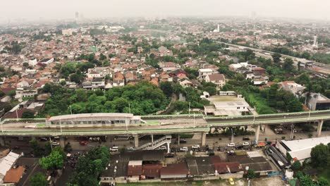 Toma-Aérea-De-Arriba-Hacia-Abajo-Que-Muestra-La-Concurrida-Autopista-Y-La-Estación-De-Tren-Cerca-Del-Distrito-De-Tugurios-De-La-Ciudad-De-Yakarta-Durante-El-Día-De-Niebla