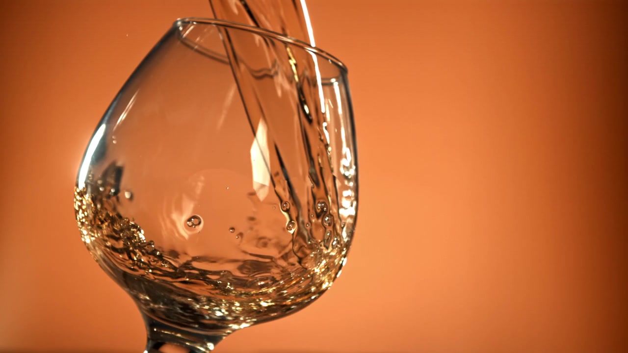 Gylden væske hældes i et cognacglas i slowmotion
