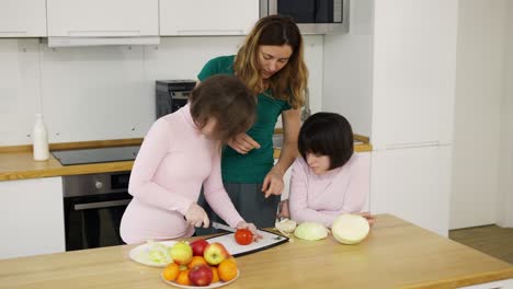 Two-girls-with-Down-Syndrome-cutting-vegetables-with-their-mother-in-kitchen-at-home