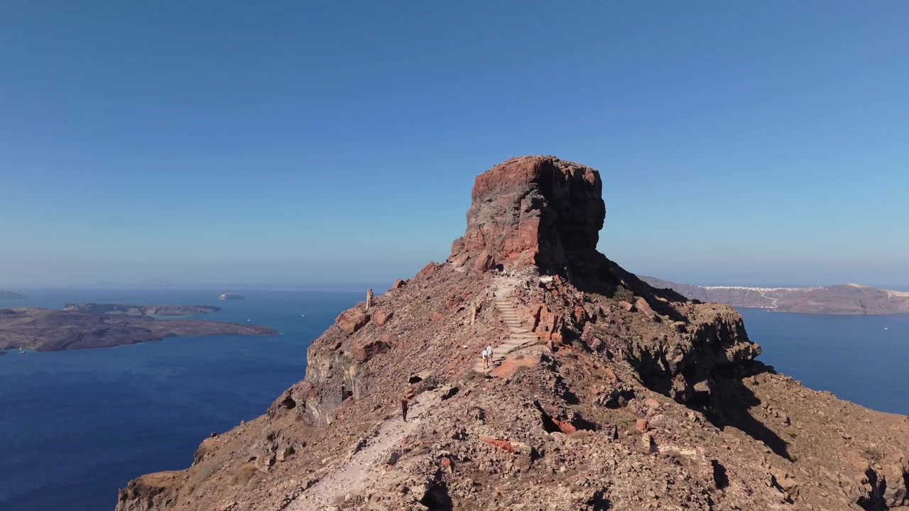 Drone in orbita intorno alla leggendaria Roccia di Skaros a Santorini. Catturato in una luminosa giornata estiva, il filmato mostra le aspre formazioni vulcaniche, le rovine con cupole blu e il vasto orizzonte egeo