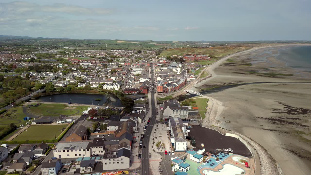 Wide-reversing aerial video of Newcastle Beach and Main Street in Newcastle, County Down in Northern Ireland in the UK. Filmed on a bright sunny day in 4K, 60fps and in Rec709 Color.