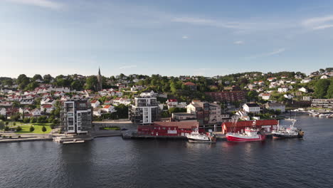 waterfront buildings with moored boats and mist on a sunny morning in arendal, norway