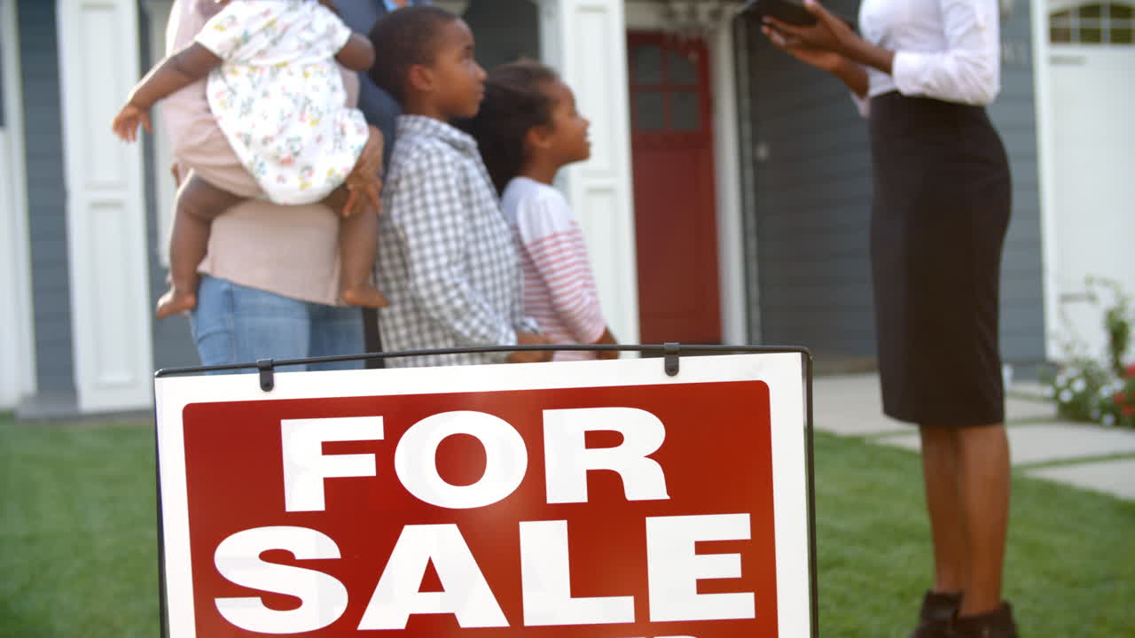 Agente immobiliare in piedi all'aperto che mostra a una famiglia una casa in vendita