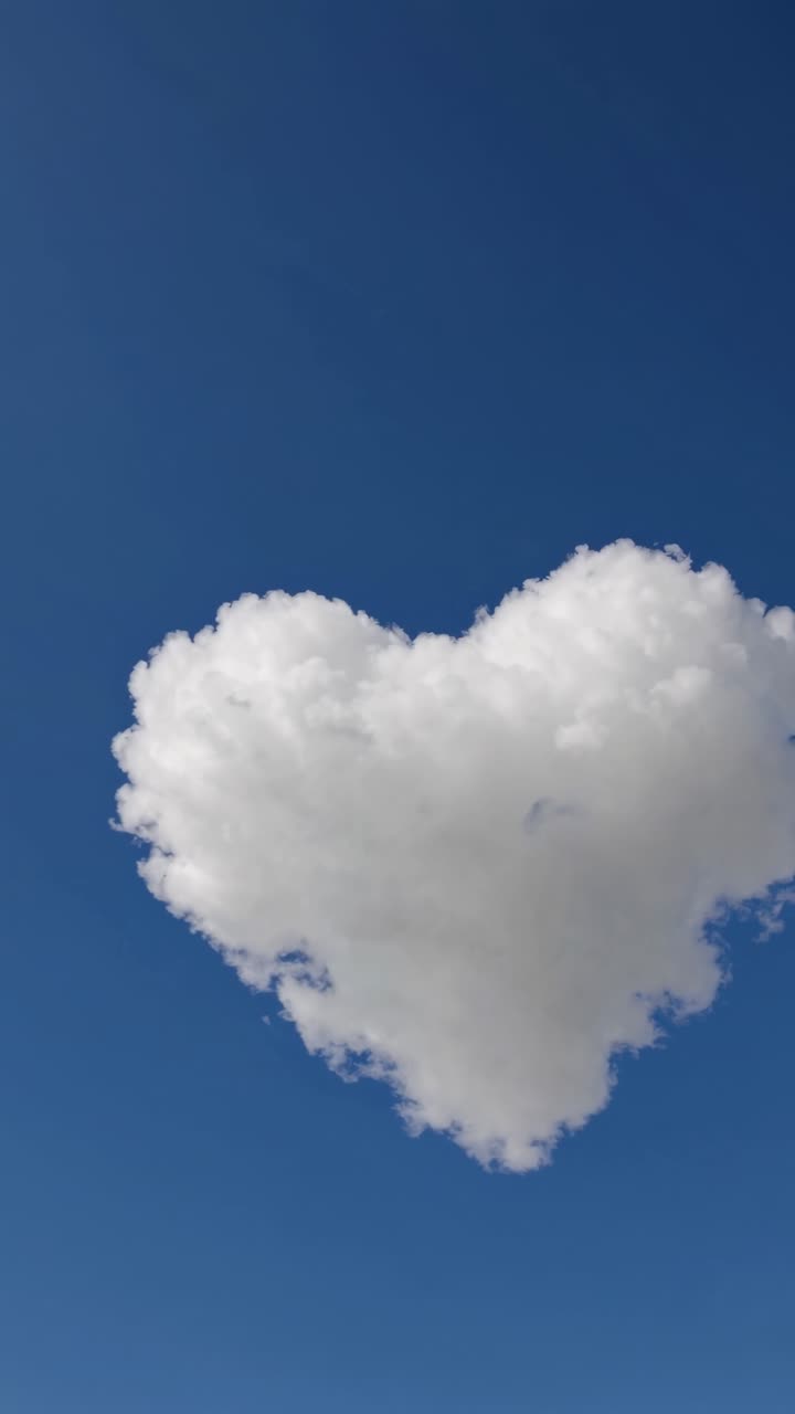 A heart-shaped cloud floats against a clear blue sky, captured from a low-angle, evoking a dreamy
