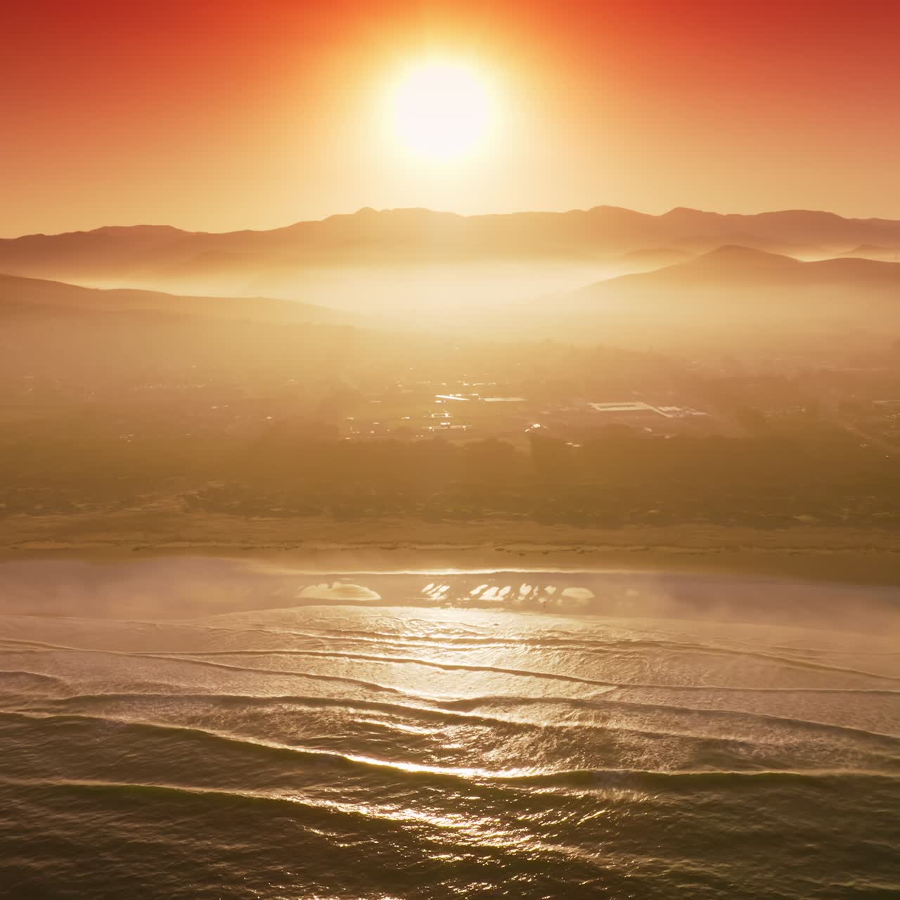 Sun reflecting in the sea water near the shore. Silhouettes of mountains and some features of city hardly seen in the rays of sunset