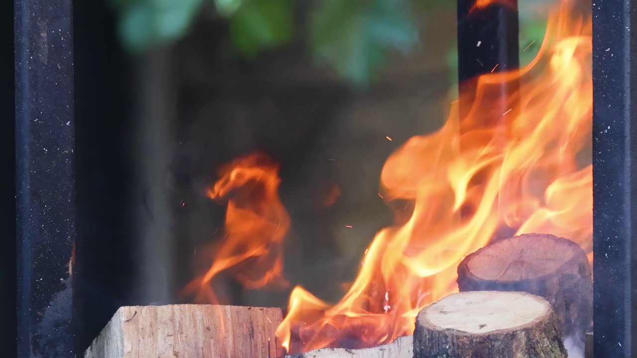 Close-up view of bright flames and smoke rising from chopped logs in a fire pit.