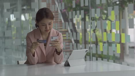 una mujer joven con una tarjeta de crédito haciendo compras en línea en una tableta. una mujer está usando una tarjeta de credito para pagar en línea con una aplicación.