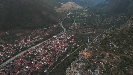 drone descends above greek flagpole and cliff to reveal town of leonidio at base of valley