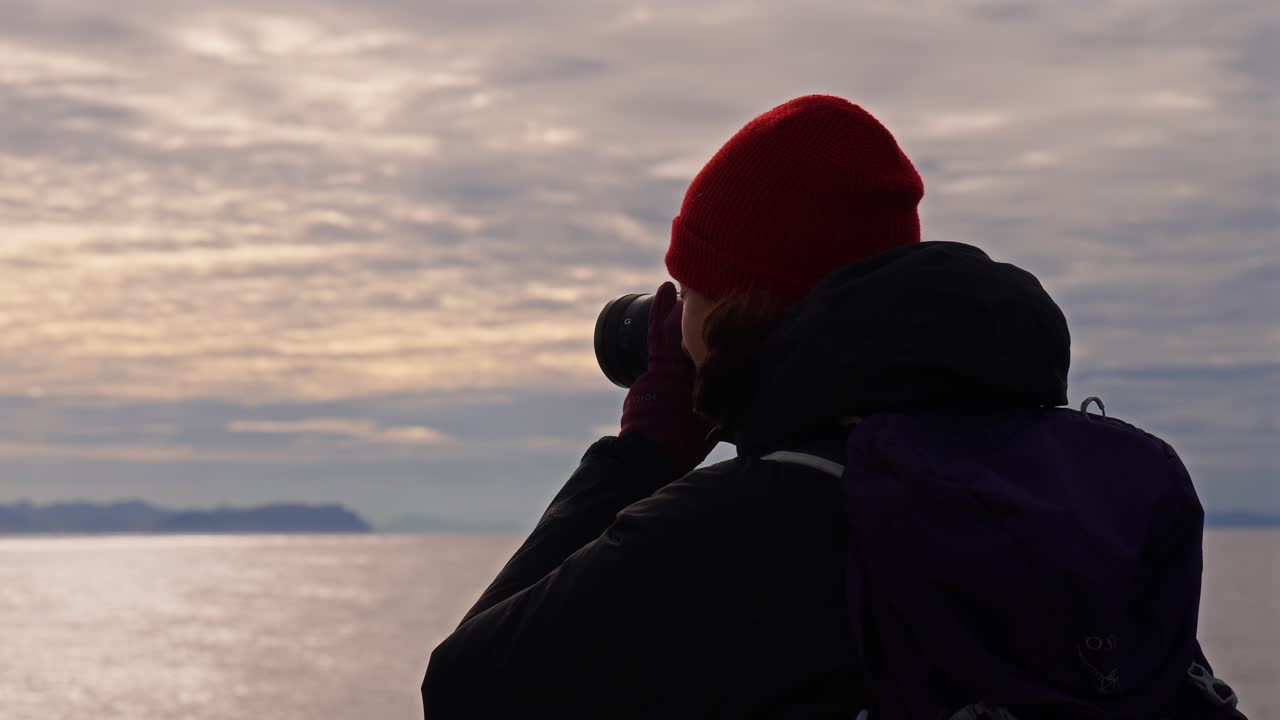 A person with a red hat is taking a photo of the scenic view over the water