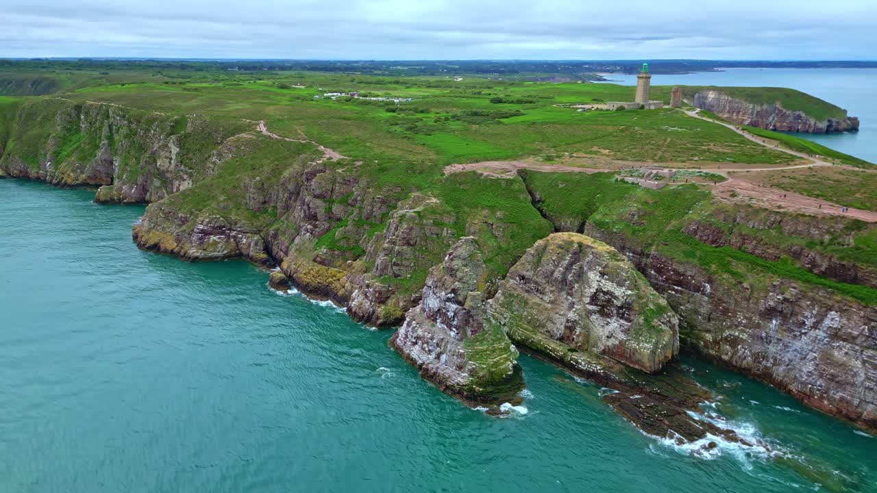 Panoramic drone movement along the Cap Fréhel peninsula with dramatic cliffs and lighthouse along vivid blue coastline, Côtes-d'Armor, Brittany, France.
