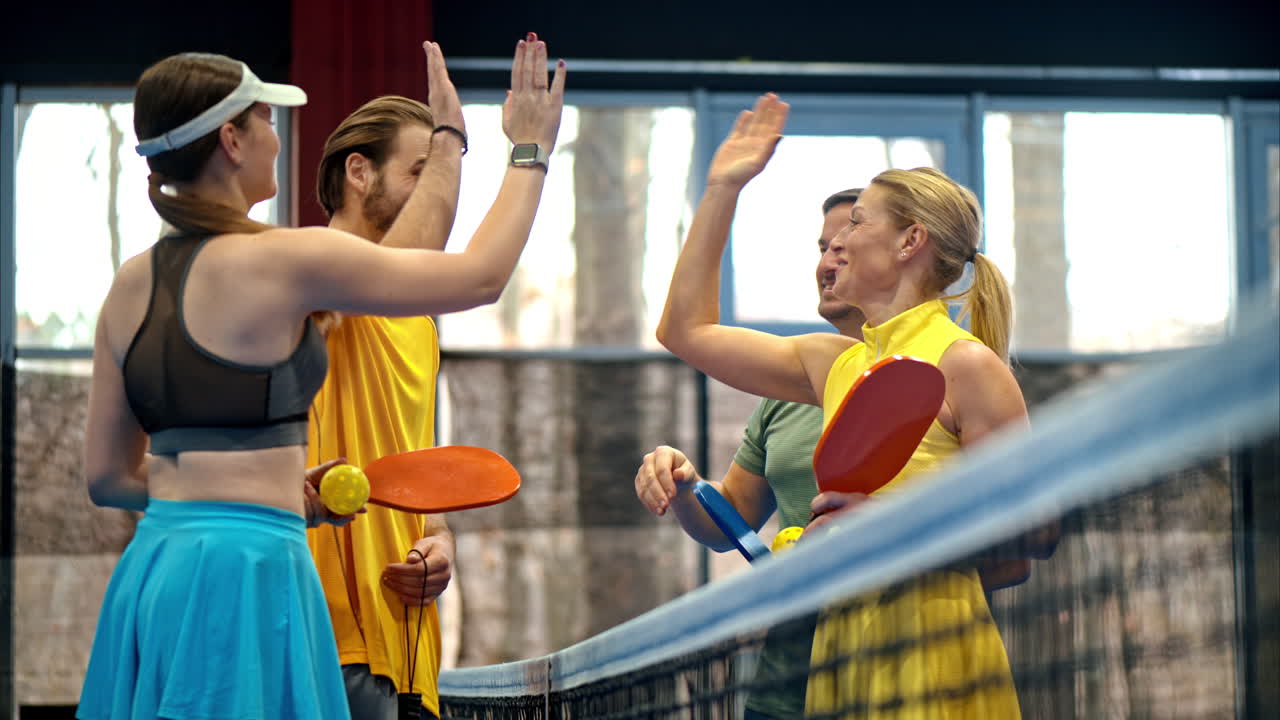 Two men and two women high-fiving after playing pickleball on a blue, inside court