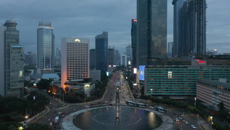 Luftaufnahme-Des-Geschäftigen-Berufsverkehrs-In-Einem-Großen-Kreisverkehr,-Umgeben-Von-Wolkenkratzern-In-Jakarta,-Indonesien