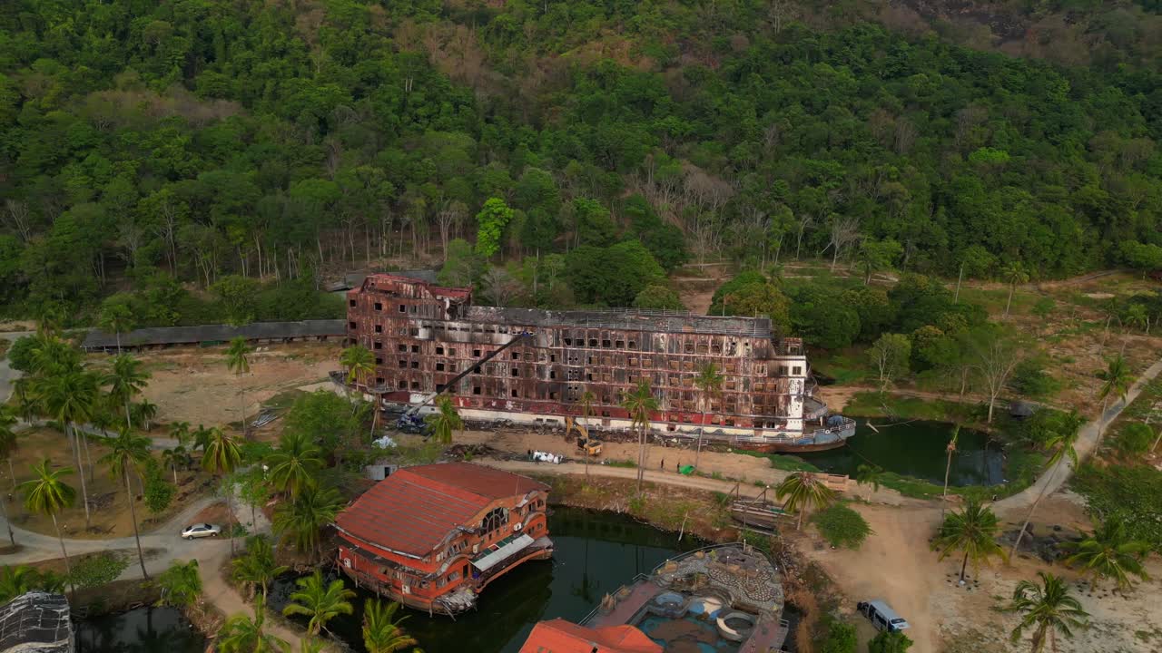 abandoned rusty ghost ship on Koh Chang on tropics island bay, Thailand, during sunset, with a crane working on it. Fabulous aerial view flight circle drone footage